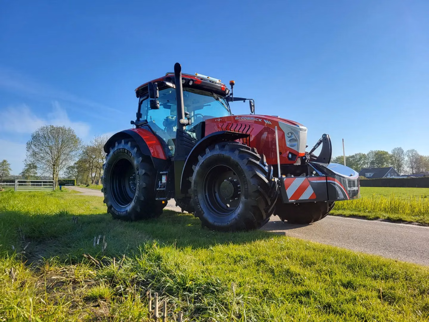 Red tractor with large tires fitted with a front weight bumper featuring LED lights and red-white safety stripes