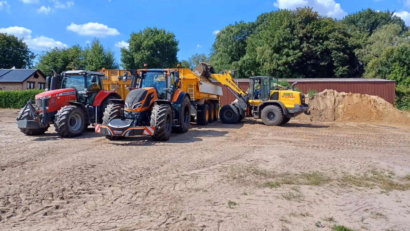Two tractors with front weight bumpers and a loader filling a yellow trailer with dirt on a sandy worksite