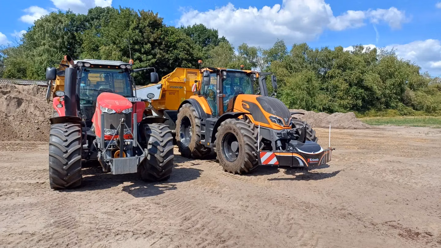 Two tractors with large tires are parked on dirt, one fitted with a black front weight bumper with red stripes.