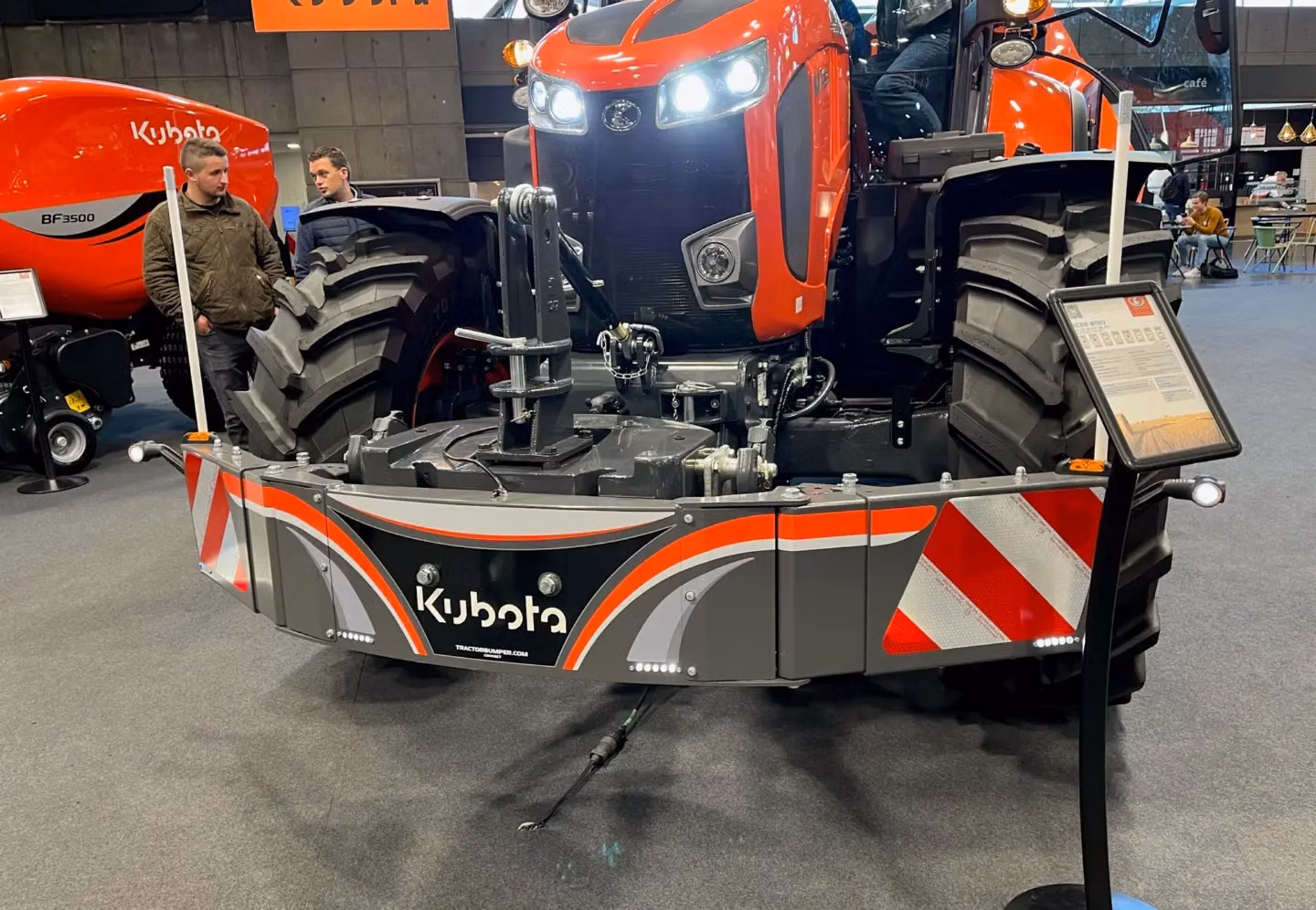 Front weight bumper with Kubota branding mounted on a large orange tractor at an indoor exhibition