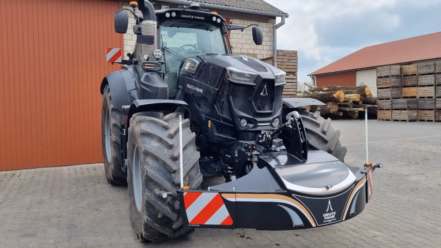 A black tractor fitted with a large front weight bumper featuring reflective red and white safety markings