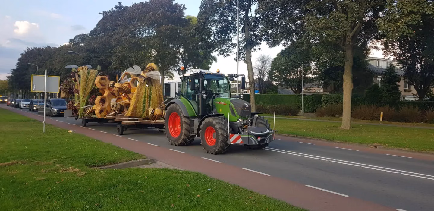 Green tractor with a front weight bumper and red wheels towing a trailer with large, colorful decorative structures