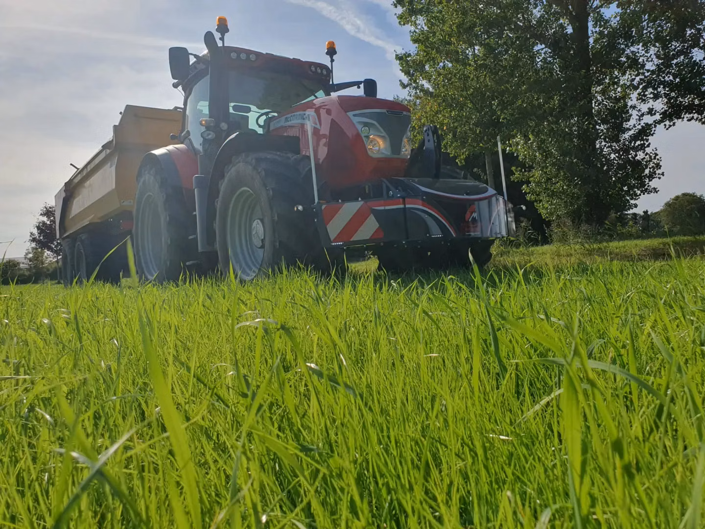 Red tractor with a front weight bumper featuring LED lights and safety markings, parked on green grass