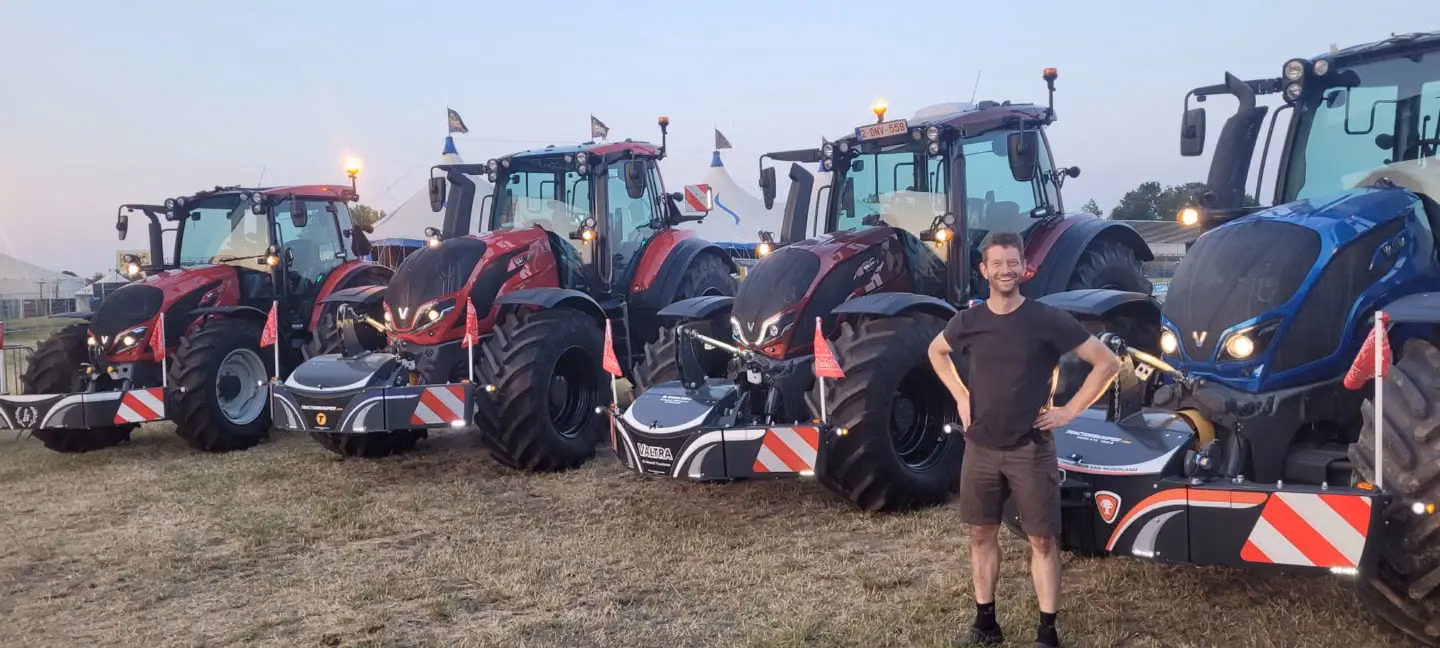 Four tractors with front weight bumpers and LED safety lights are parked on grass with a person smiling in front