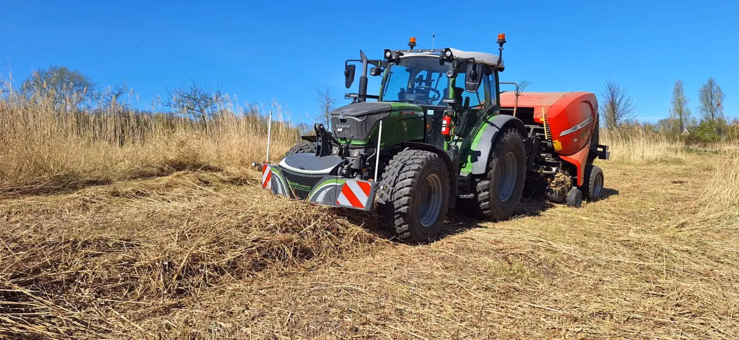 Tractor with a front weight bumper featuring reflective stripes, operating in a dry grassy field under a clear sky