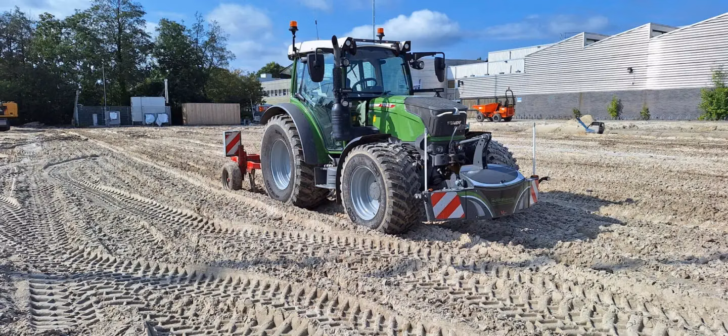 Large green tractor with front weight bumper featuring lights and safety markings, parked on a dirt construction site