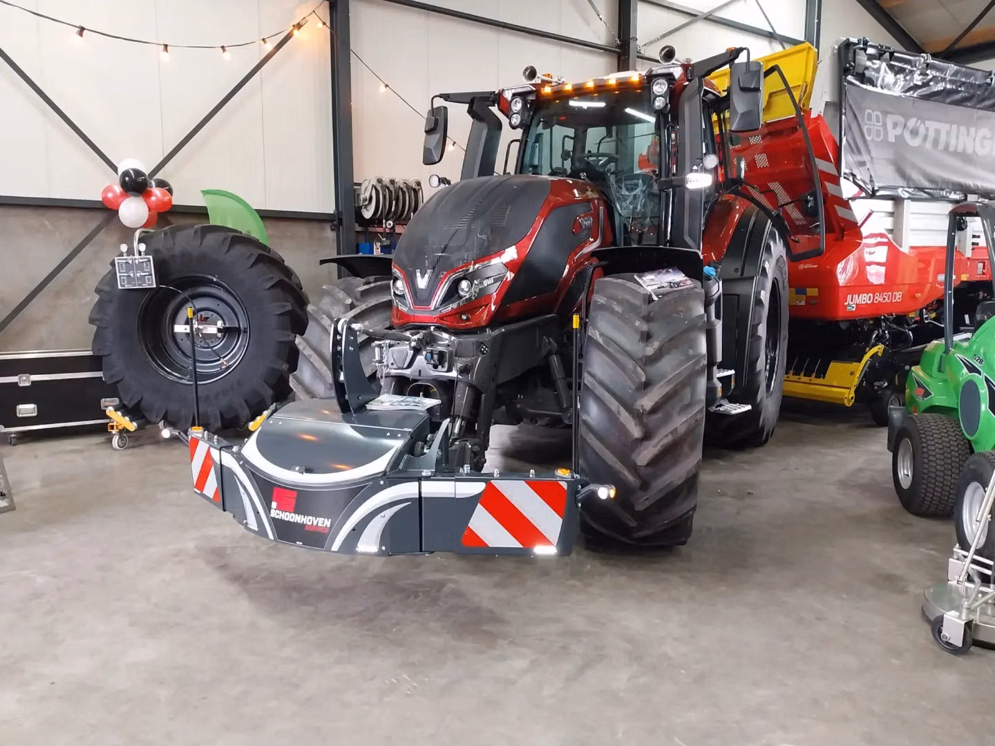 A red tractor indoors with a front weight bumper attached, surrounded by equipment and machinery