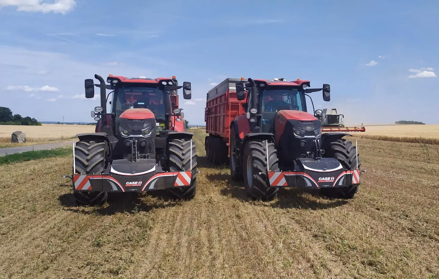 Two red tractors in a field, each fitted with a CASE IH front weight bumper, with one pulling a red trailer.