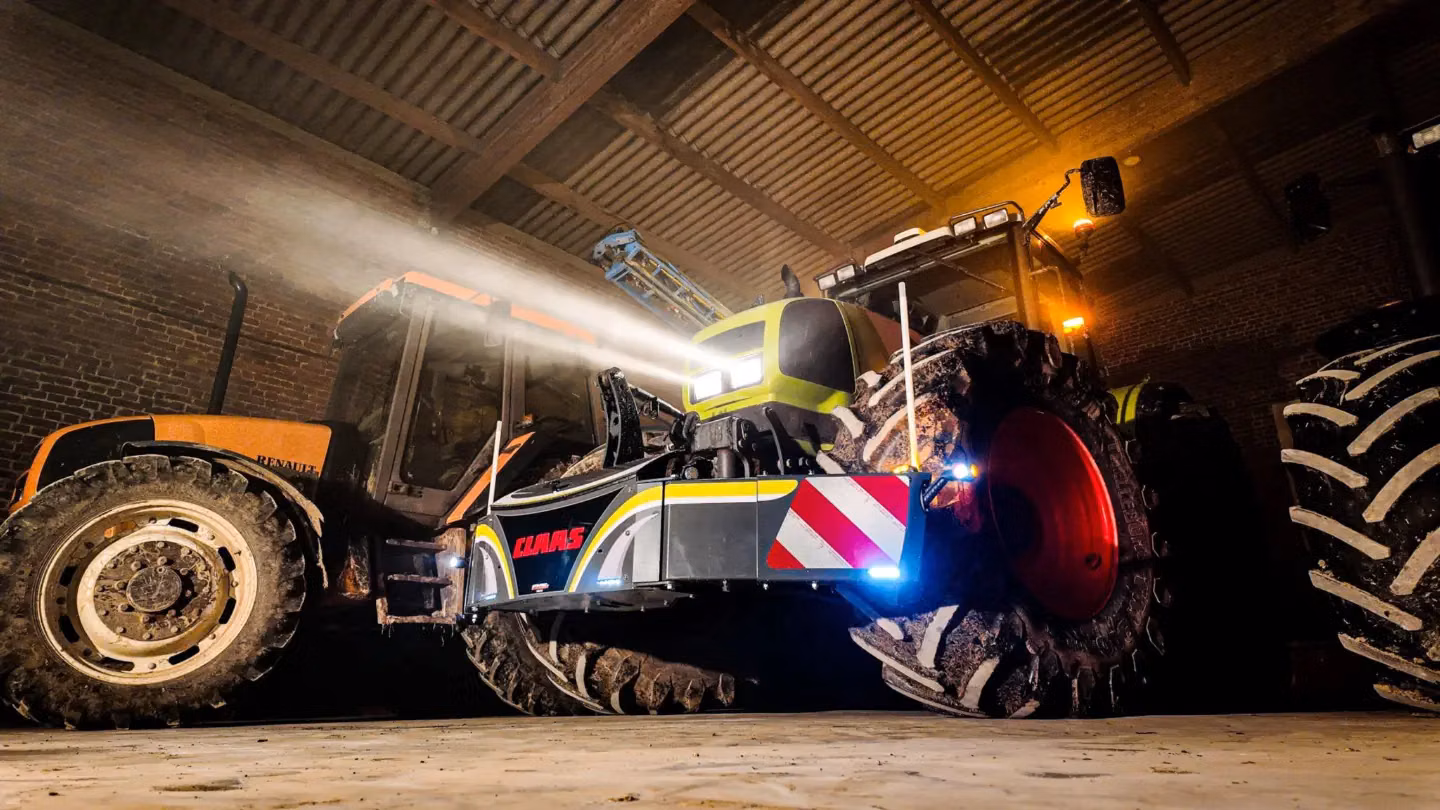 A front weight bumper with reflectors and CLAAS branding mounted on a tractor inside a barn with headlights on