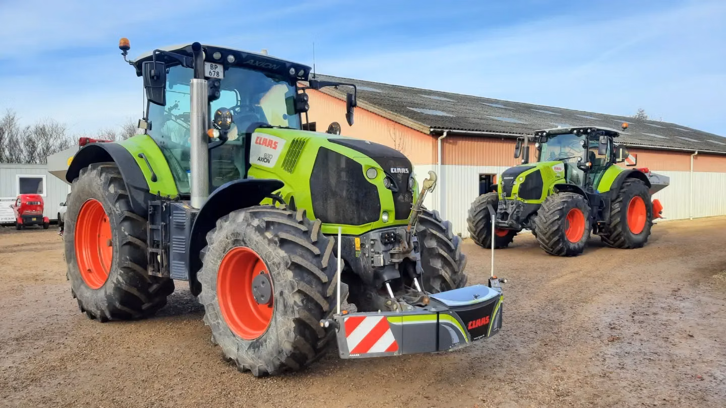 Two green tractors with red wheels parked on a dirt lot, both equipped with front weight bumpers marked CLAAS