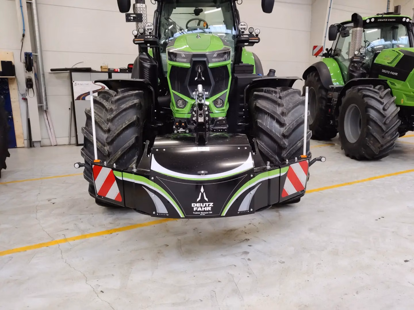 A green tractor with a Deutz-Fahr branded front weight bumper and reflective safety markings in an indoor garage
