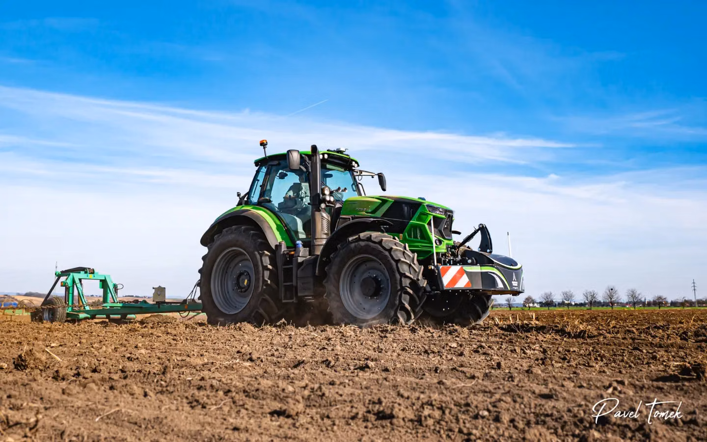 Green tractor with a large front weight bumper working in a plowed field under a blue sky