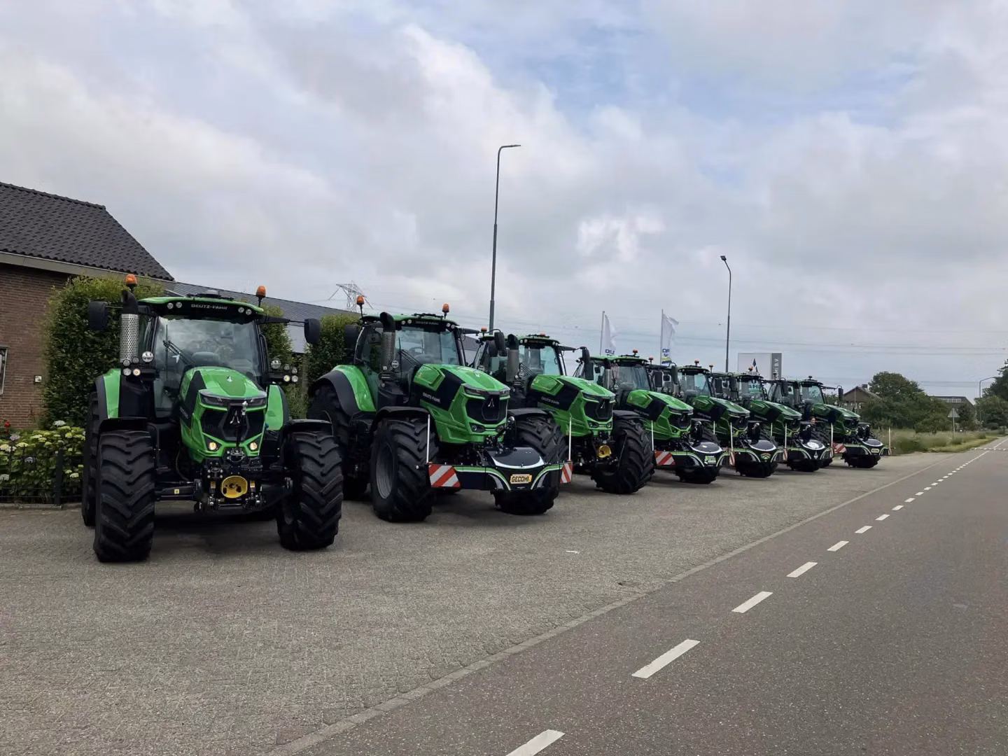 A row of green tractors with front weight bumpers parked on the side of a paved road