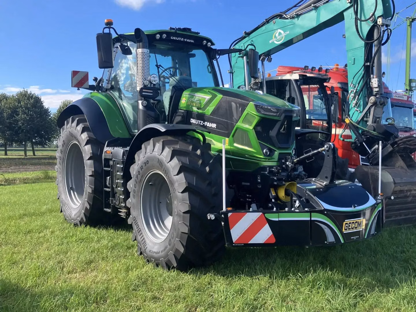 Green tractor with large tires is fitted with a black front weight bumper that has reflective red and white stripes