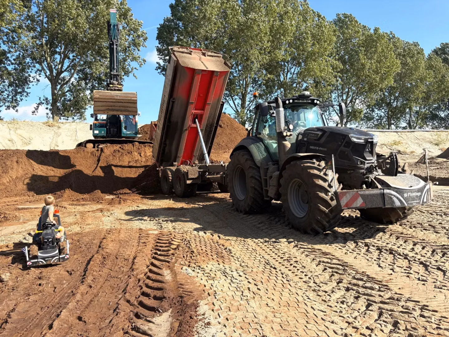 A Deutz-Fahr tractor with a front weight bumper on a construction site beside a tipper and an excavator