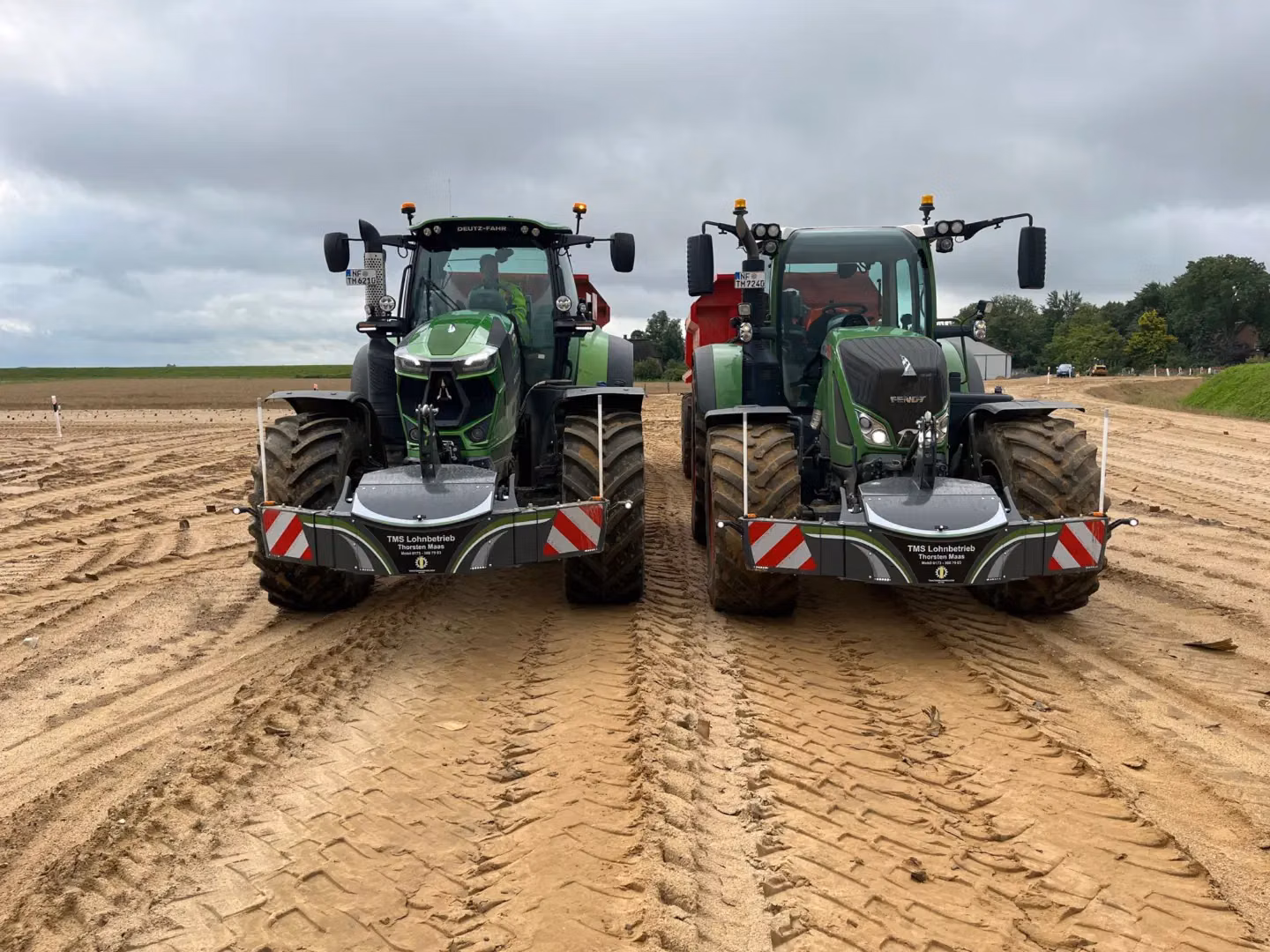 Two green tractors on a dirt field, each fitted with a front weight bumper featuring red and white reflective stripes
