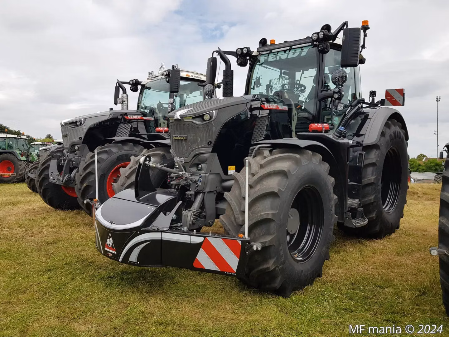 Large black tractor with a mounted front weight bumper, parked on grass next to similar tractors in a row