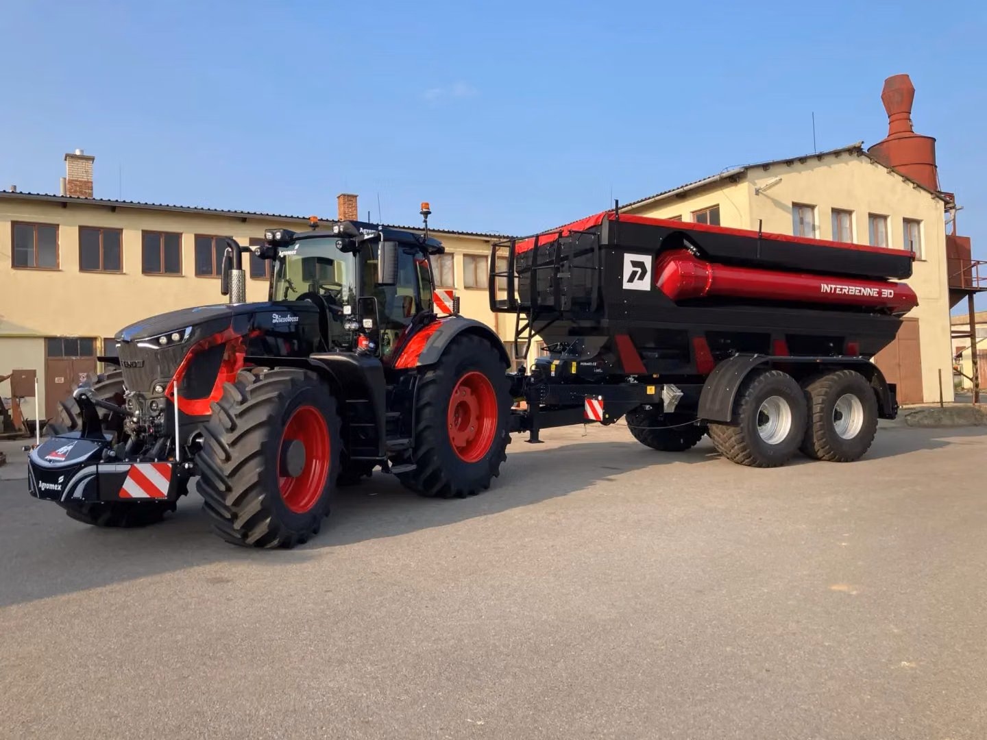 Black and red tractor with a front weight bumper attached, pulling a large black and red trailer on pavement