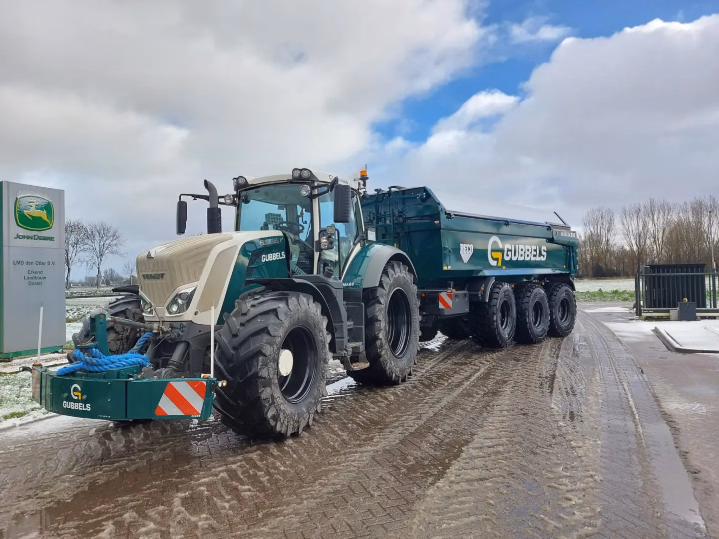 Green front weight bumper with reflectors and lights mounted on a tractor parked on a wet, partly snowy road