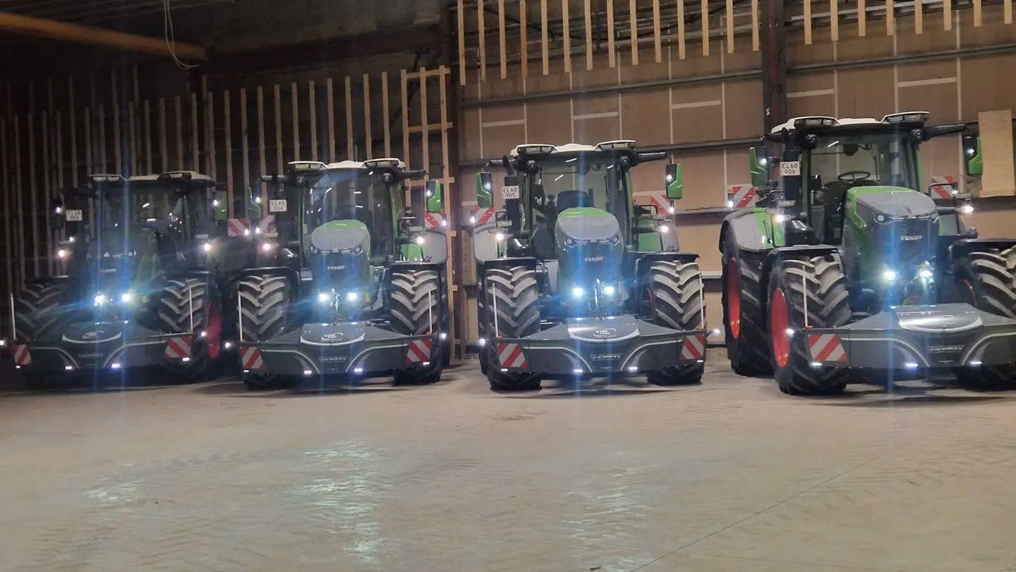 Five green tractors indoors, each fitted with large front weight bumpers with integrated lights and safety markings