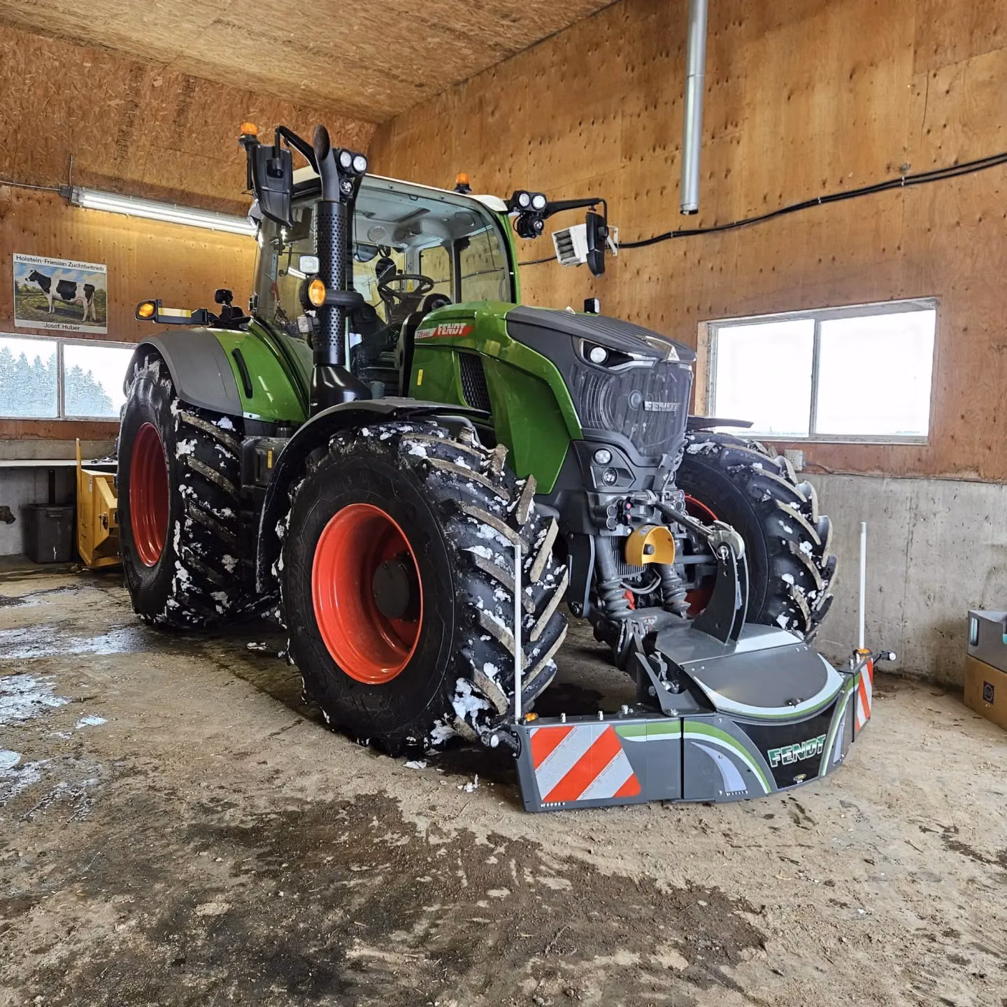 A green tractor with red wheels is parked indoors, fitted with a front weight bumper featuring reflective safety markings