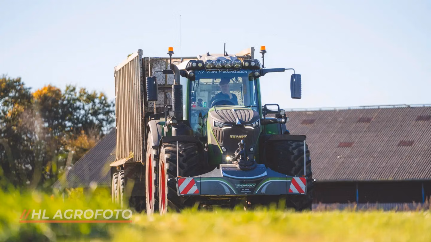 A tractor with a front weight bumper featuring warning stripes and lights is parked on grass in front of a barn.