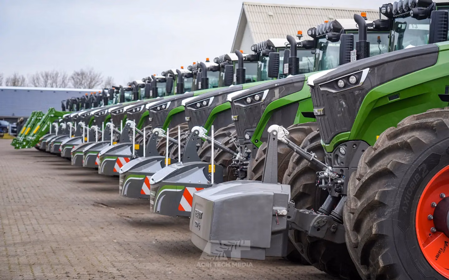 Row of green tractors fitted with grey front weight bumpers featuring safety markings and integrated lights