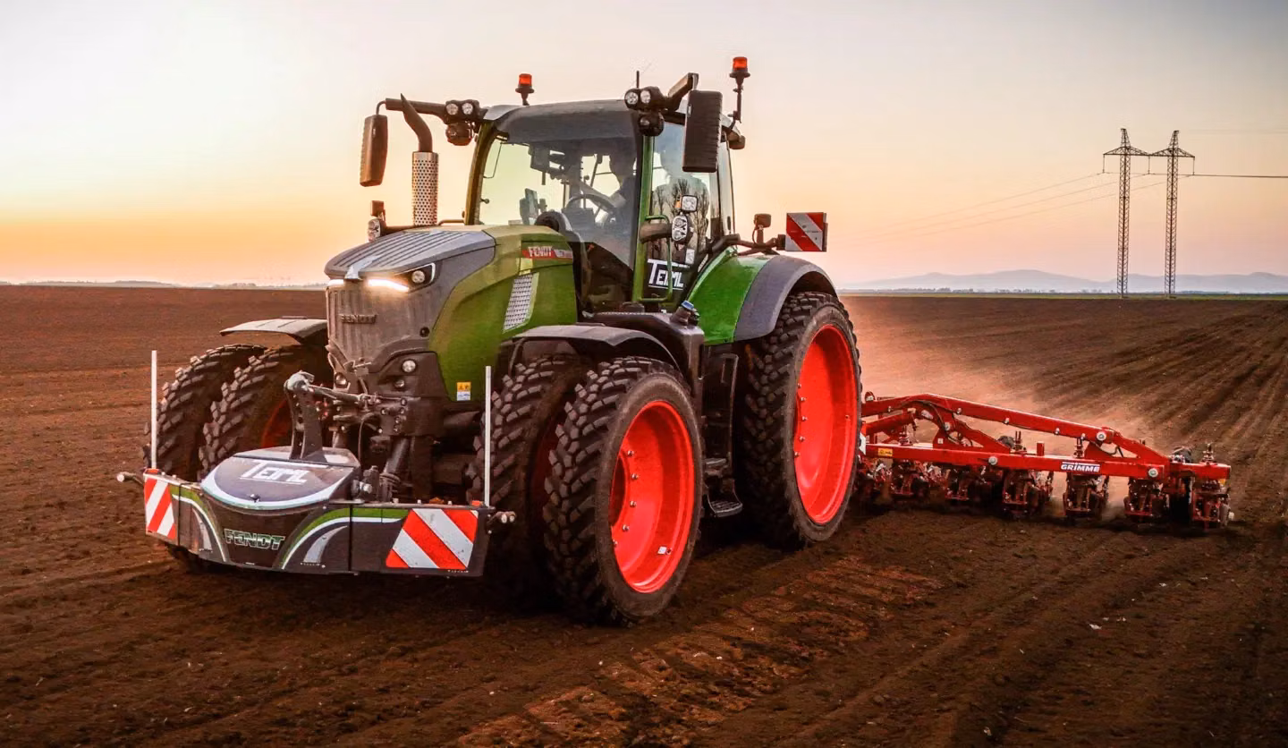 A green tractor with a front weight bumper featuring red and white safety stripes works on a field at sunset