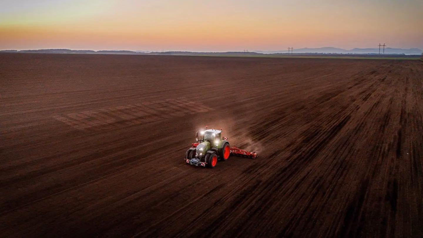 Tractor with illuminated front weight bumper and large tires working a wide, freshly tilled field at dusk