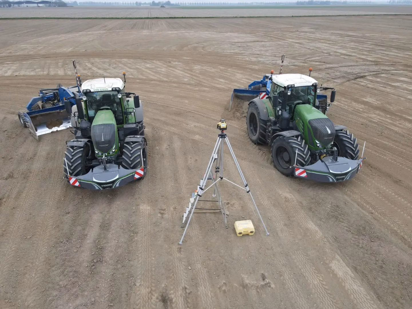 Two green tractors with front weight bumpers are parked on a dirt field with a tripod and equipment between them