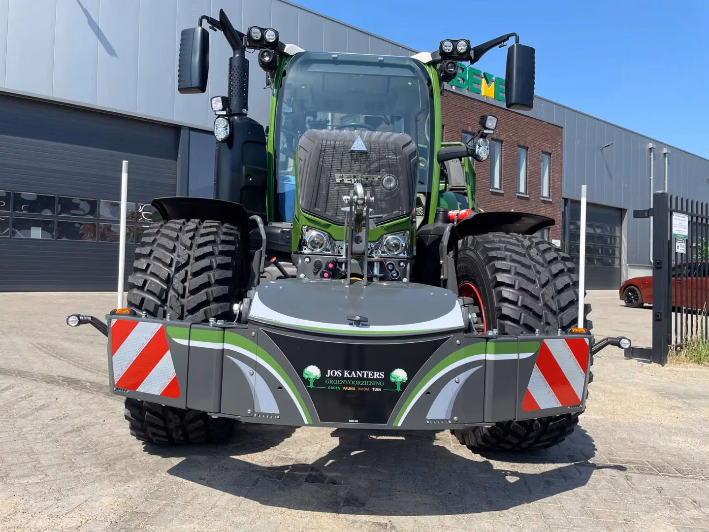 A green tractor with a large front weight bumper featuring warning stripes, lights, and safety markers