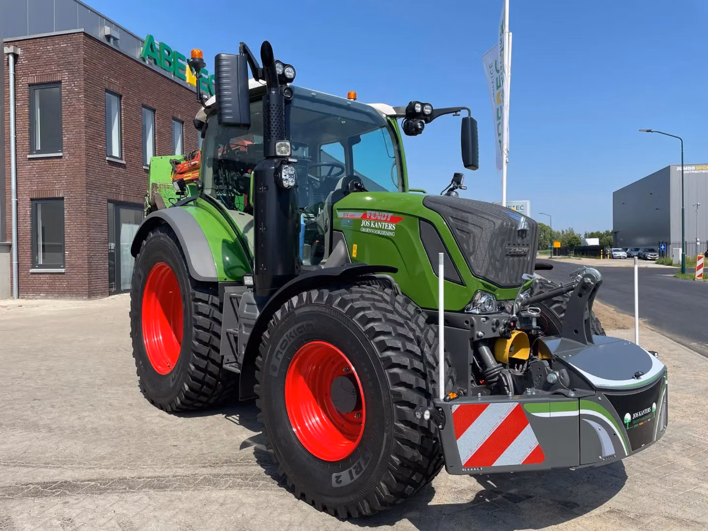 Green tractor with a front weight bumper featuring red and white safety stripes, parked on a paved lot