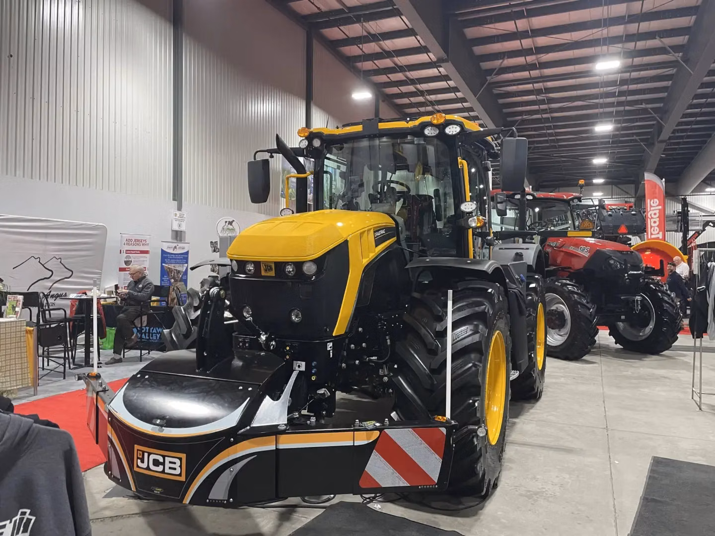 A yellow and black tractor fitted with a JCB front weight bumper is displayed indoors at an exhibition.