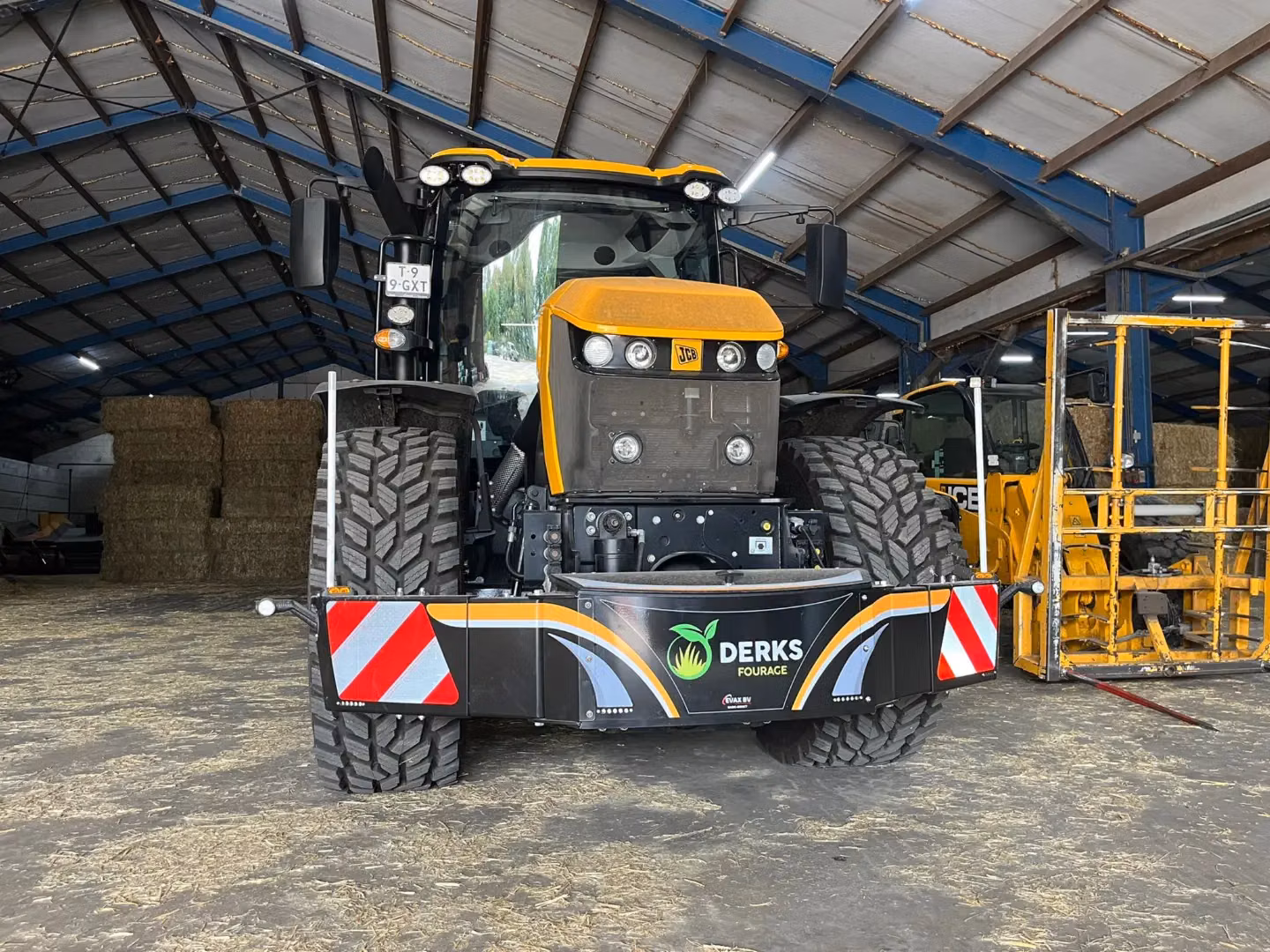 A large yellow tractor in a barn equipped with a front weight bumper labeled Derks Fourage with warning stripes