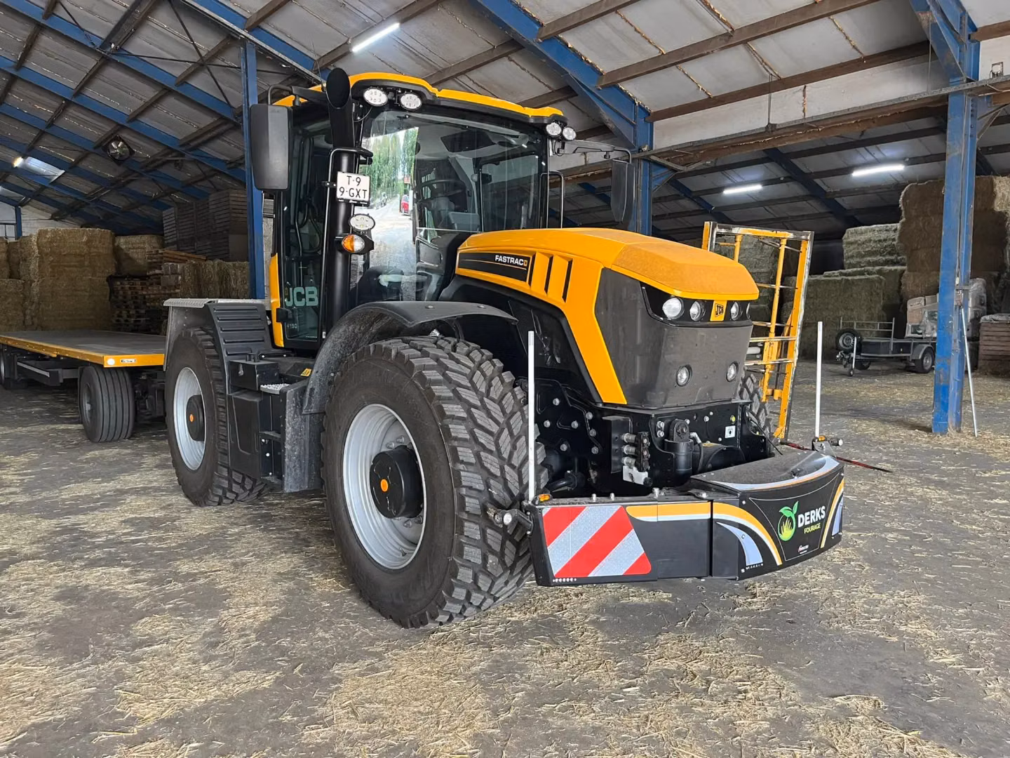 Yellow and black tractor with a large front weight bumper featuring red and white safety stripes in a hay barn