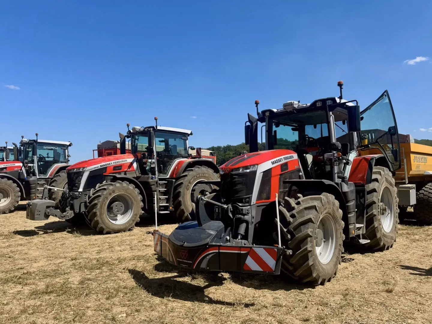 Three red tractors equipped with front weight bumpers are parked on a dry field under a clear blue sky