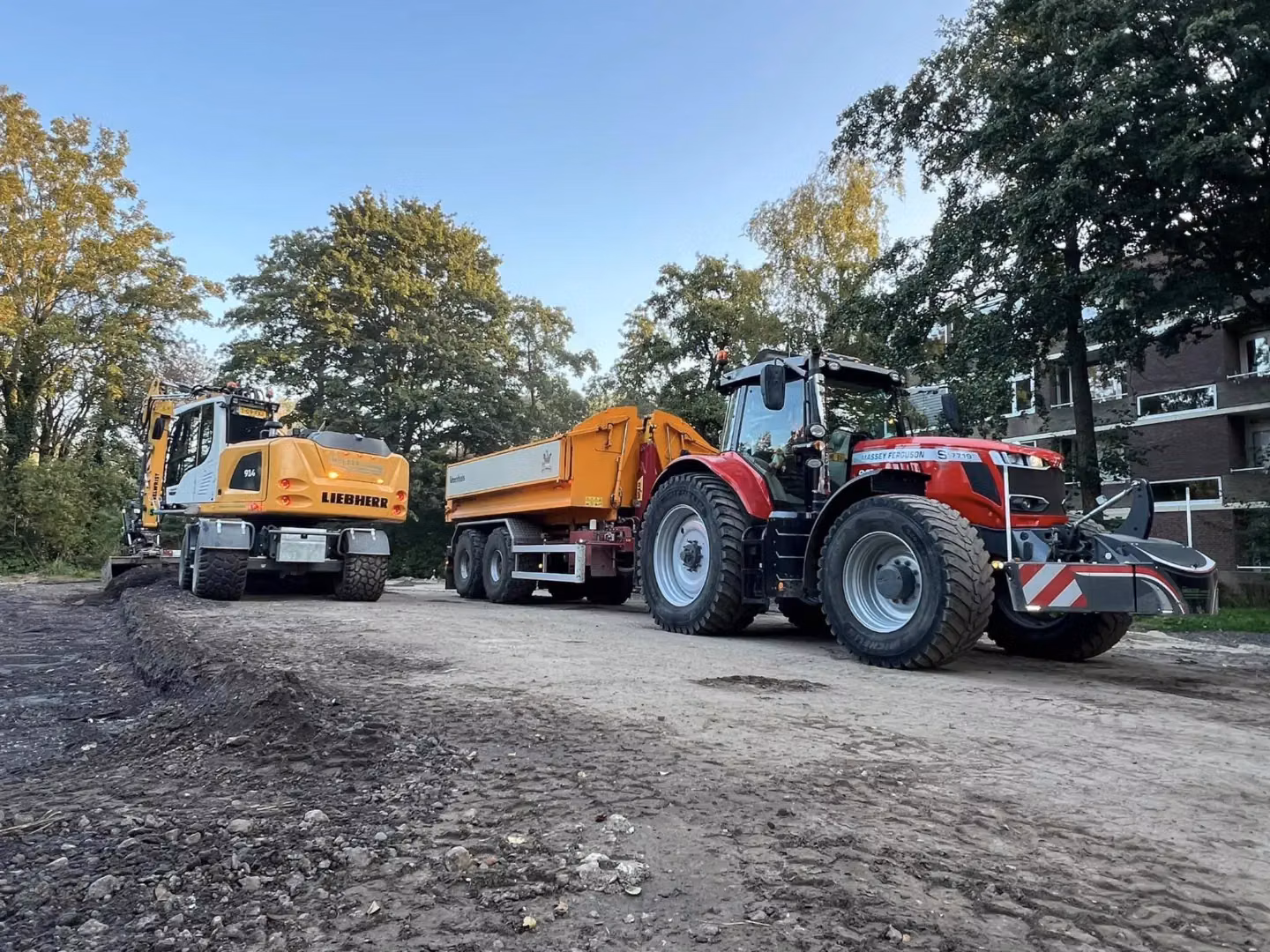 Red tractor with large tires, a trailer attached, and a front weight bumper parked on a dirt road near construction equipment