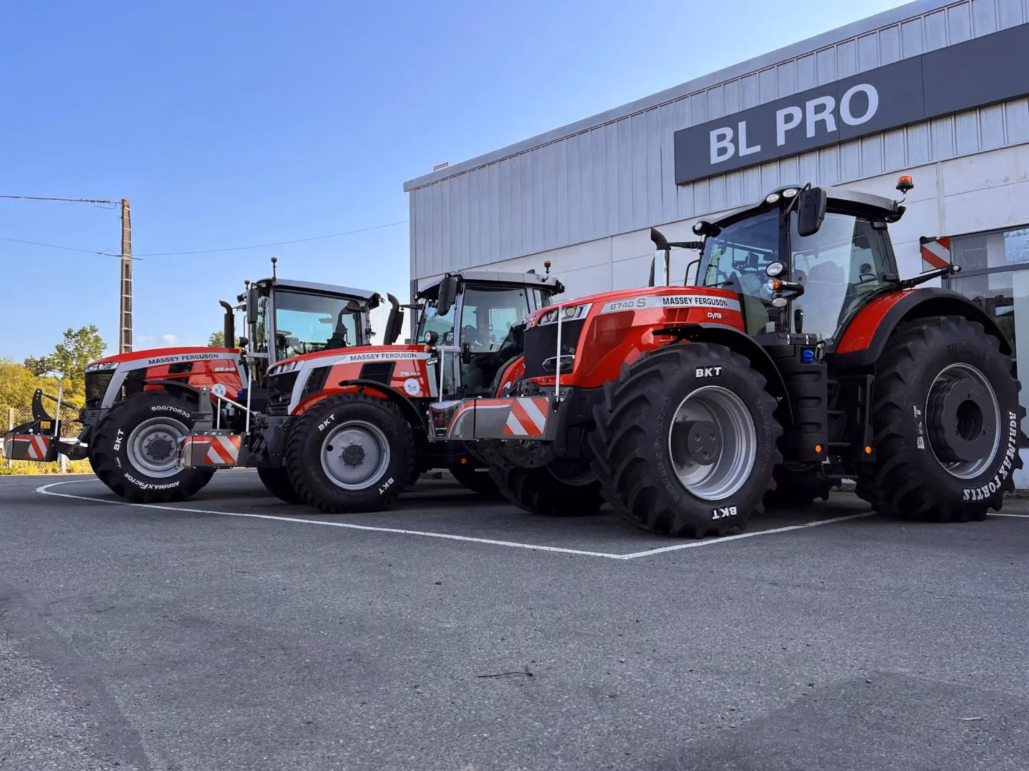 Three red Massey Ferguson tractors equipped with front weight bumpers parked outside a building labeled BL PRO