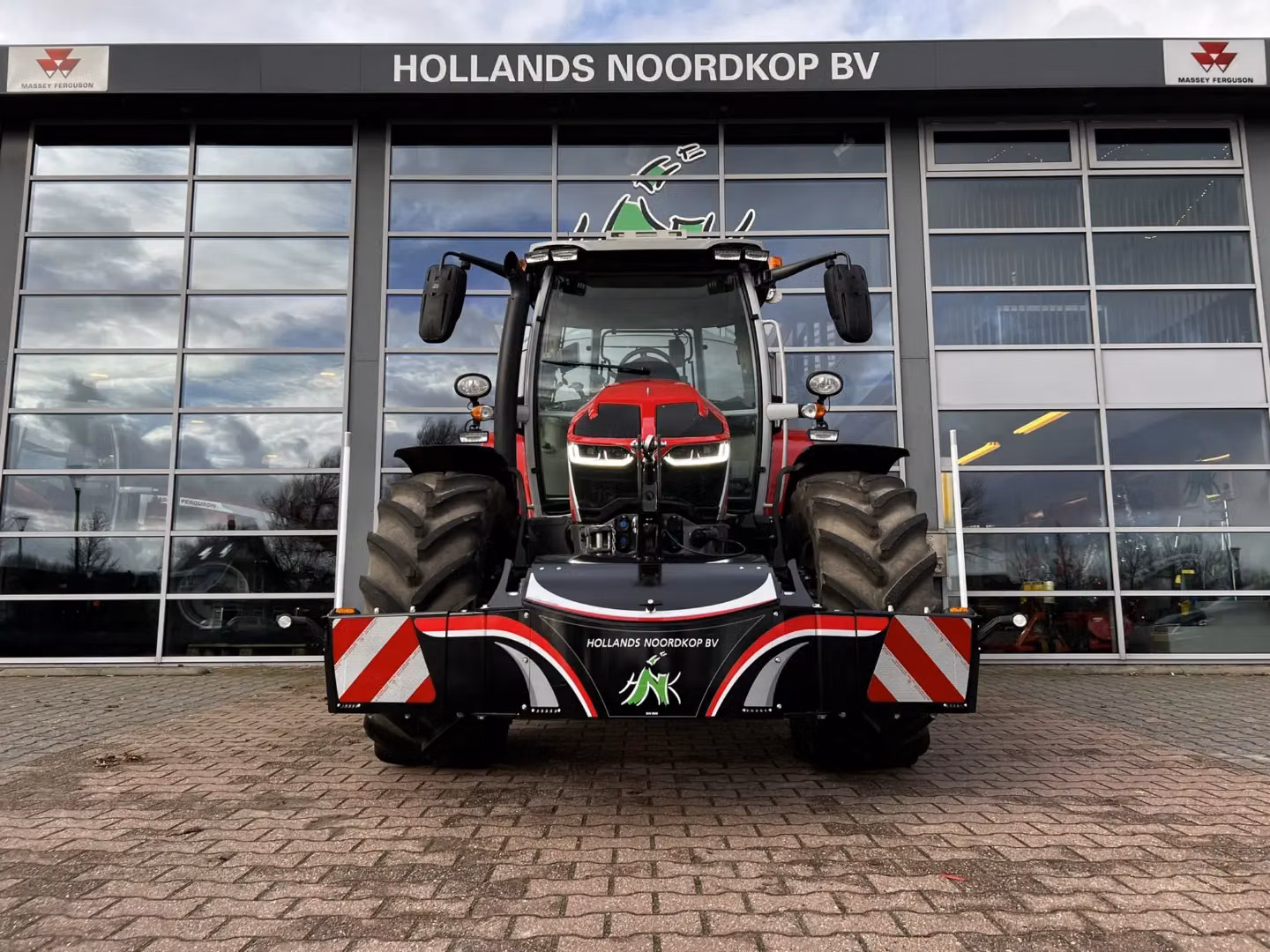 Red tractor with a large front weight bumper featuring LED lights and reflective safety stripes, parked on brick pavement