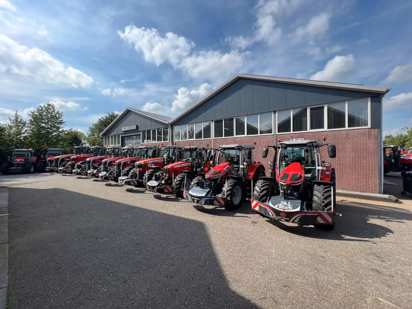 Several red tractors with front weight bumpers are lined up outside a building on a sunny day