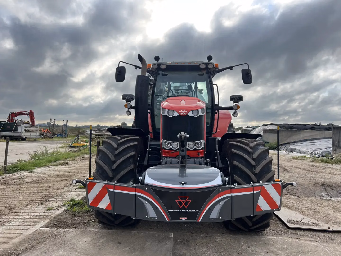 Red Massey Ferguson tractor with a mounted front weight bumper featuring LED lights and safety markings, outdoors on a farm