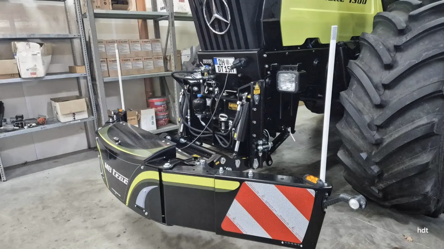 Front weight bumper with reflective red and white stripes mounted on a green tractor parked in a workshop
