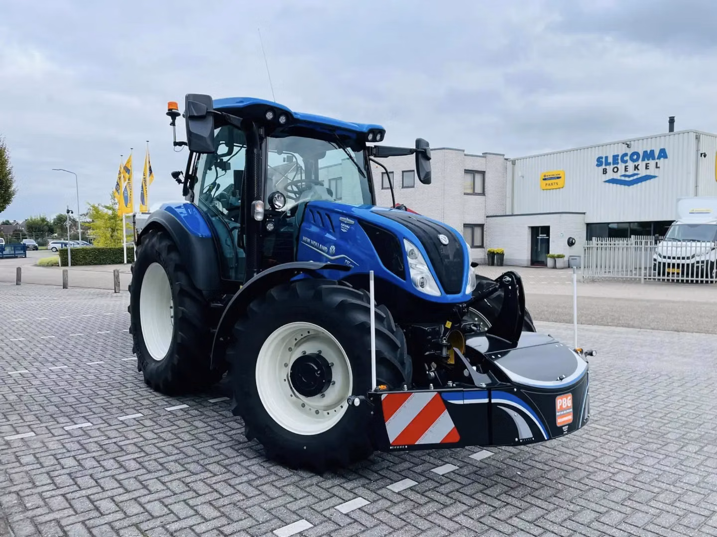 Blue tractor with large front weight bumper featuring red and white reflective stripes on a paved lot