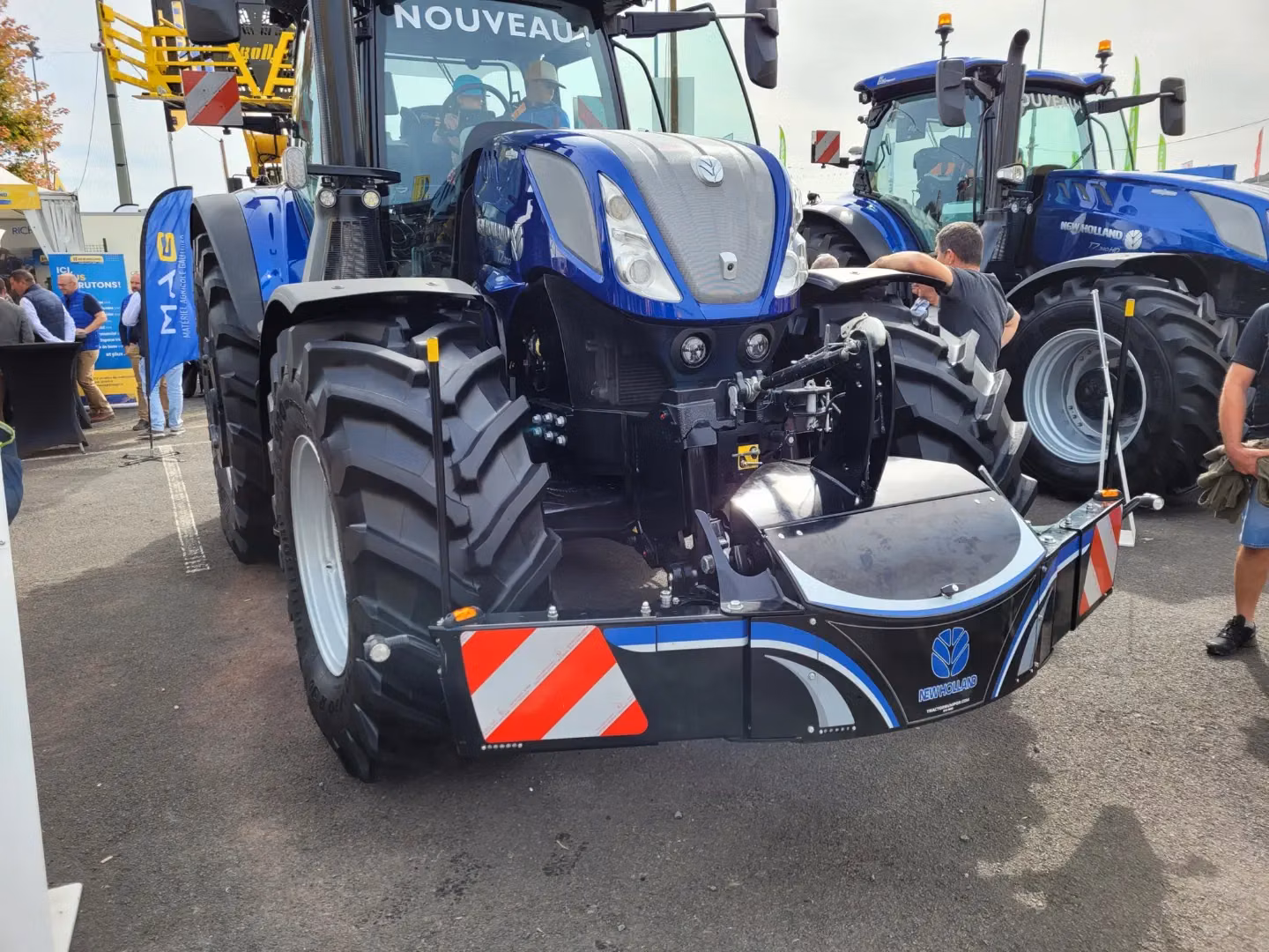 Large blue tractor equipped with a black front weight bumper featuring reflective red and white stripes