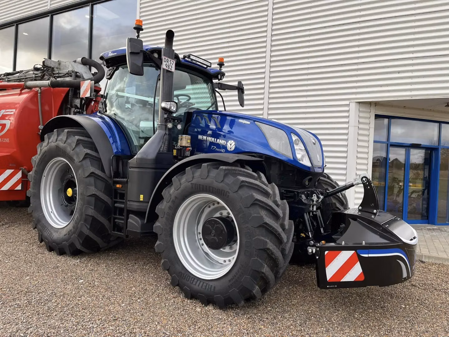 A blue tractor with a black front weight bumper featuring reflective red and white stripes on a gravel surface