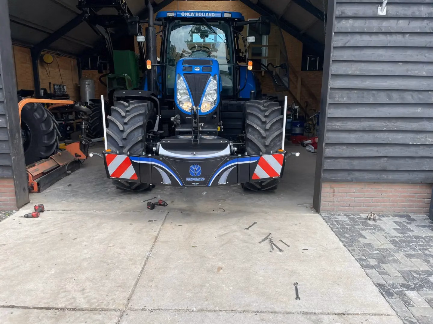 Blue tractor with a front weight bumper featuring LED lights and red-white reflective stripes in a shed.