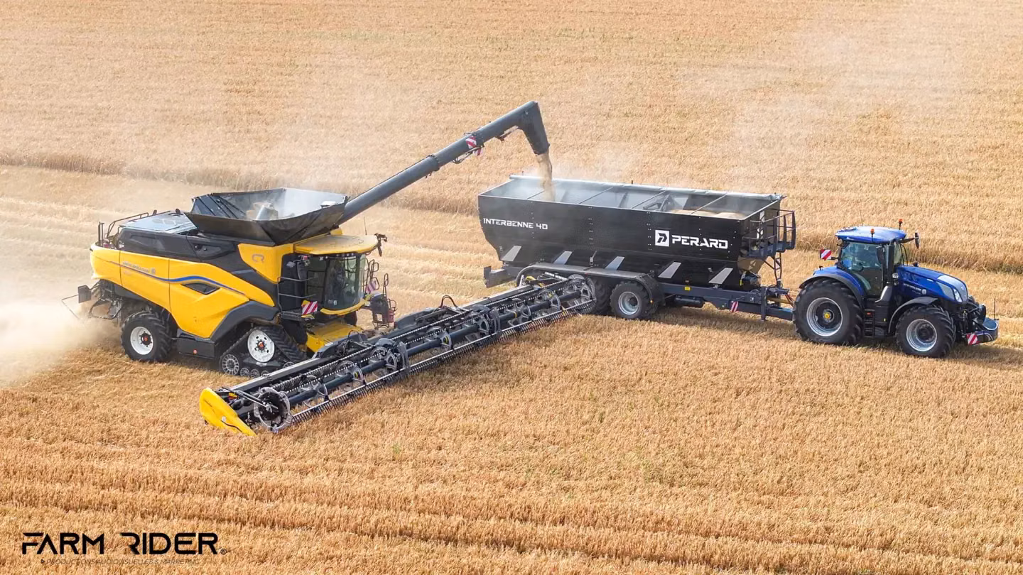 A blue tractor with a front weight bumper tows a grain trailer beside a yellow combine in a harvested field