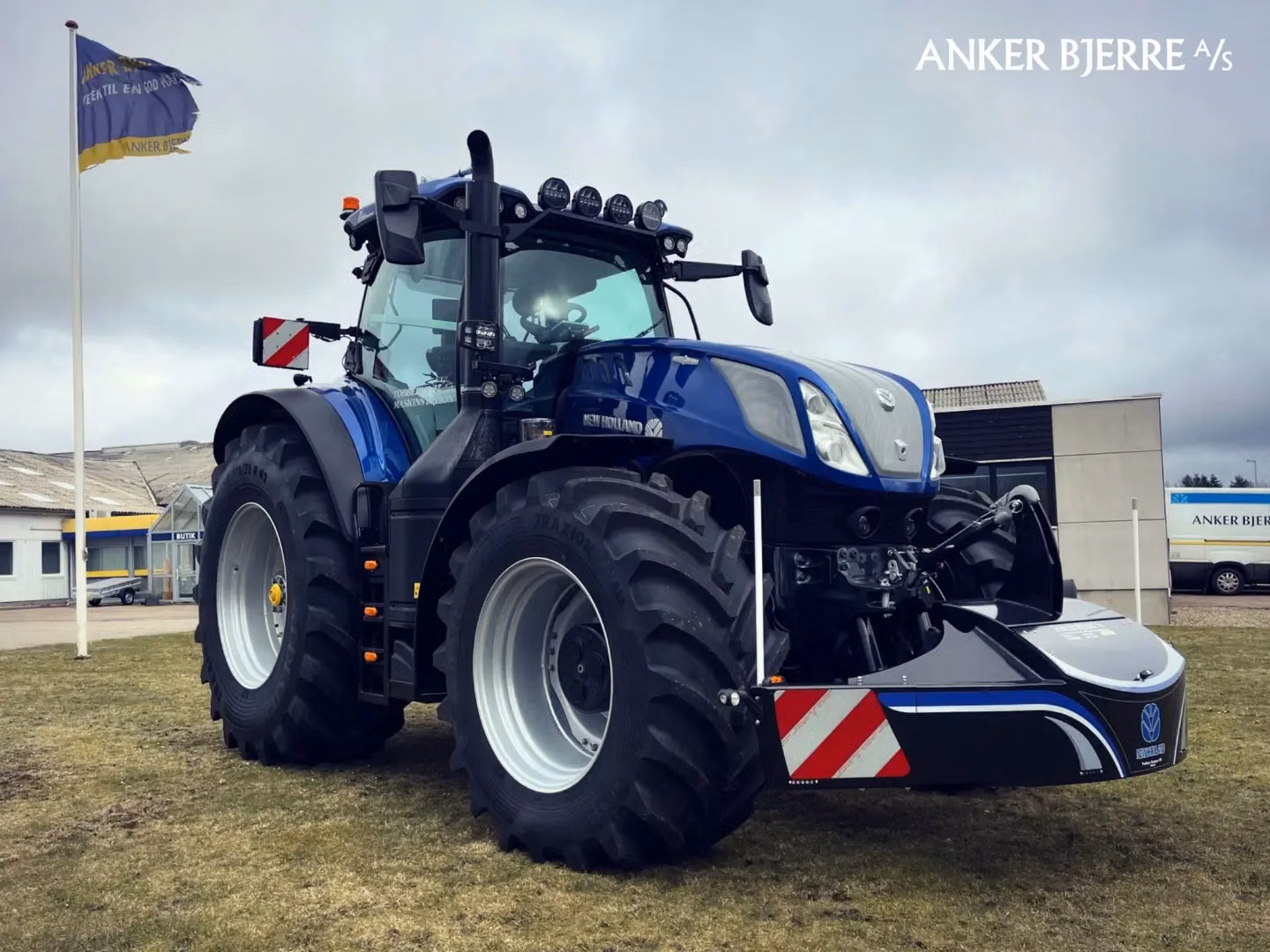 A blue tractor fitted with a large black front weight bumper featuring red and white reflective stripes
