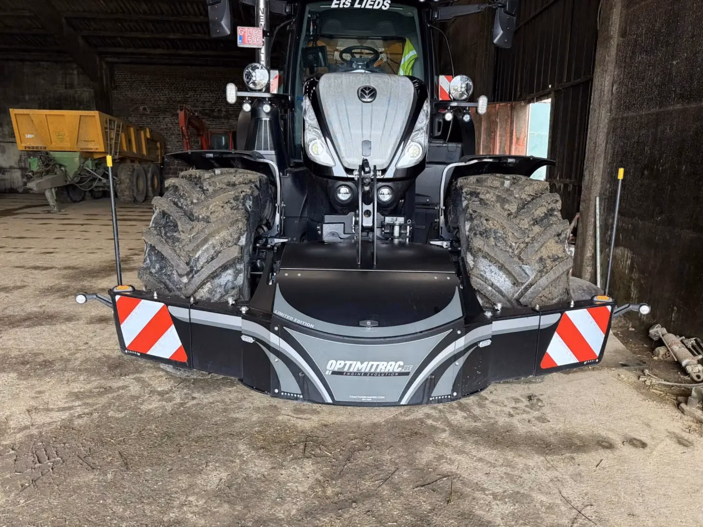 A tractor equipped with a large front weight bumper featuring reflective red and white panels and warning poles