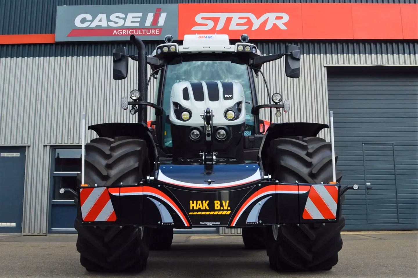 Front view of a tractor with large tires and a mounted front weight bumper featuring red and white warning stripes